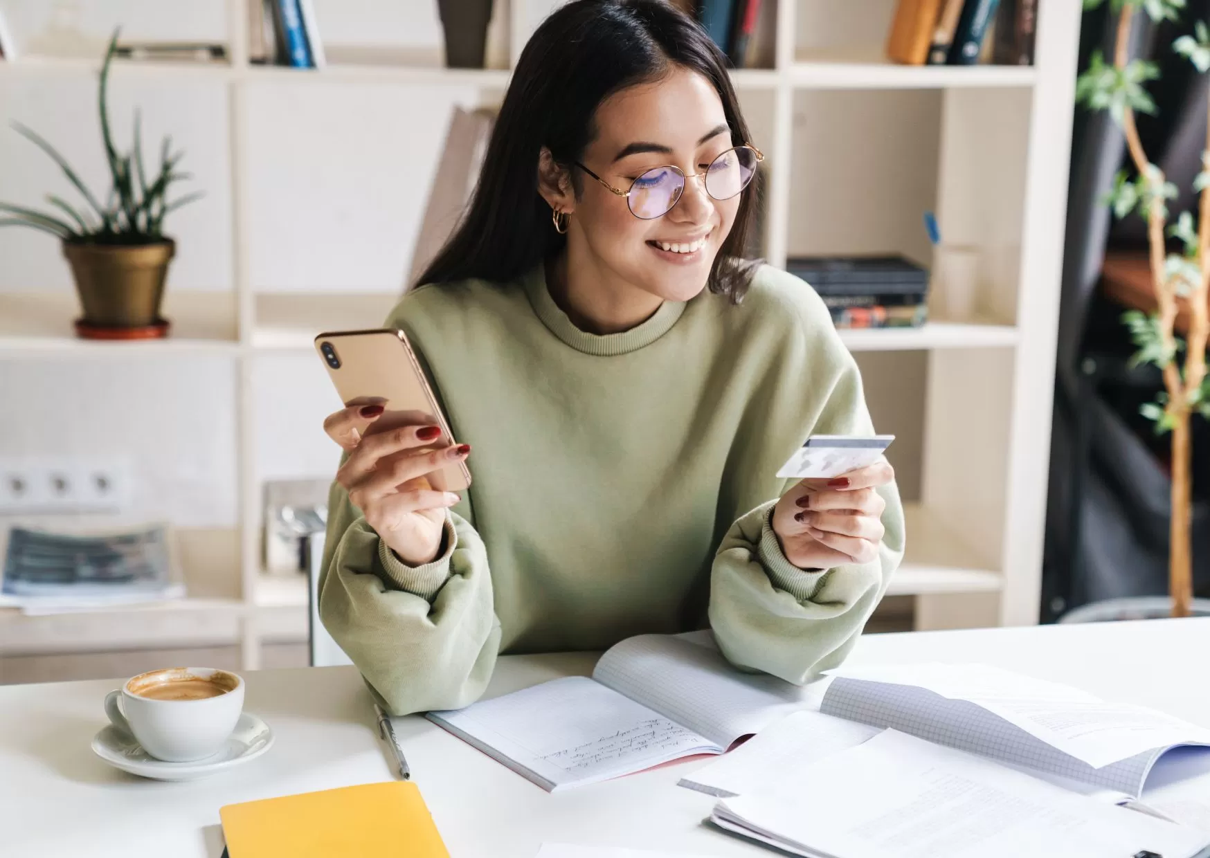 Young woman in a sweater looking at her credit card and phone